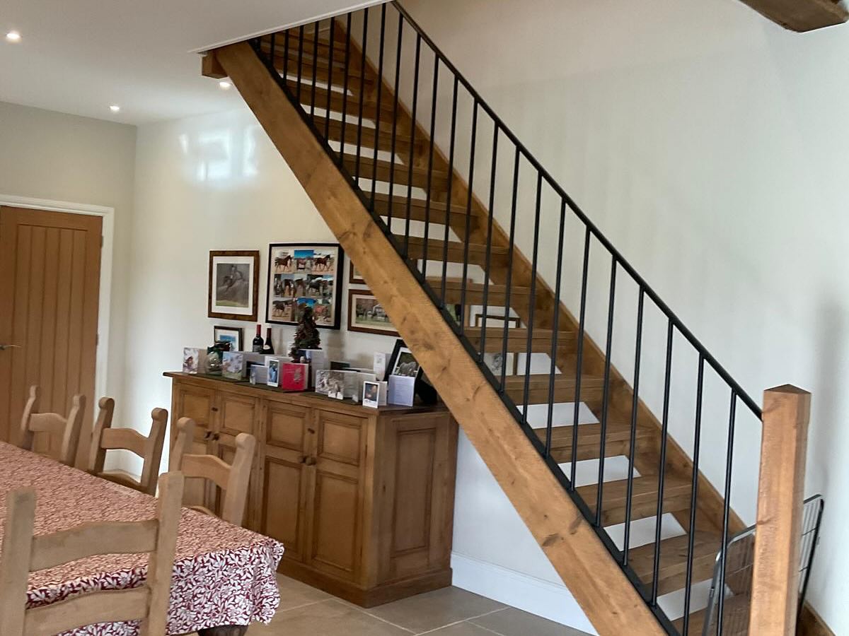 Oak staircase with a black metal balustrade beside a dining table