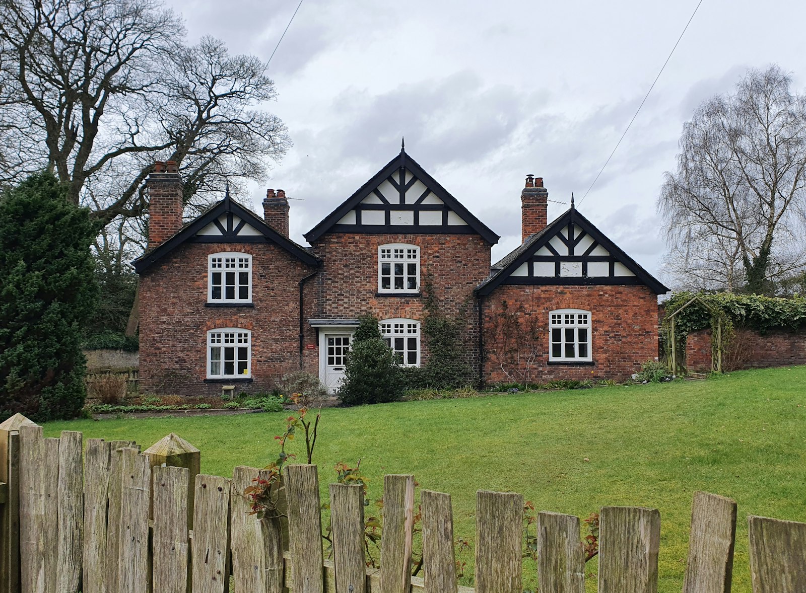 Red-brick farmhouse with timber gables, white sash windows, and several chimneys